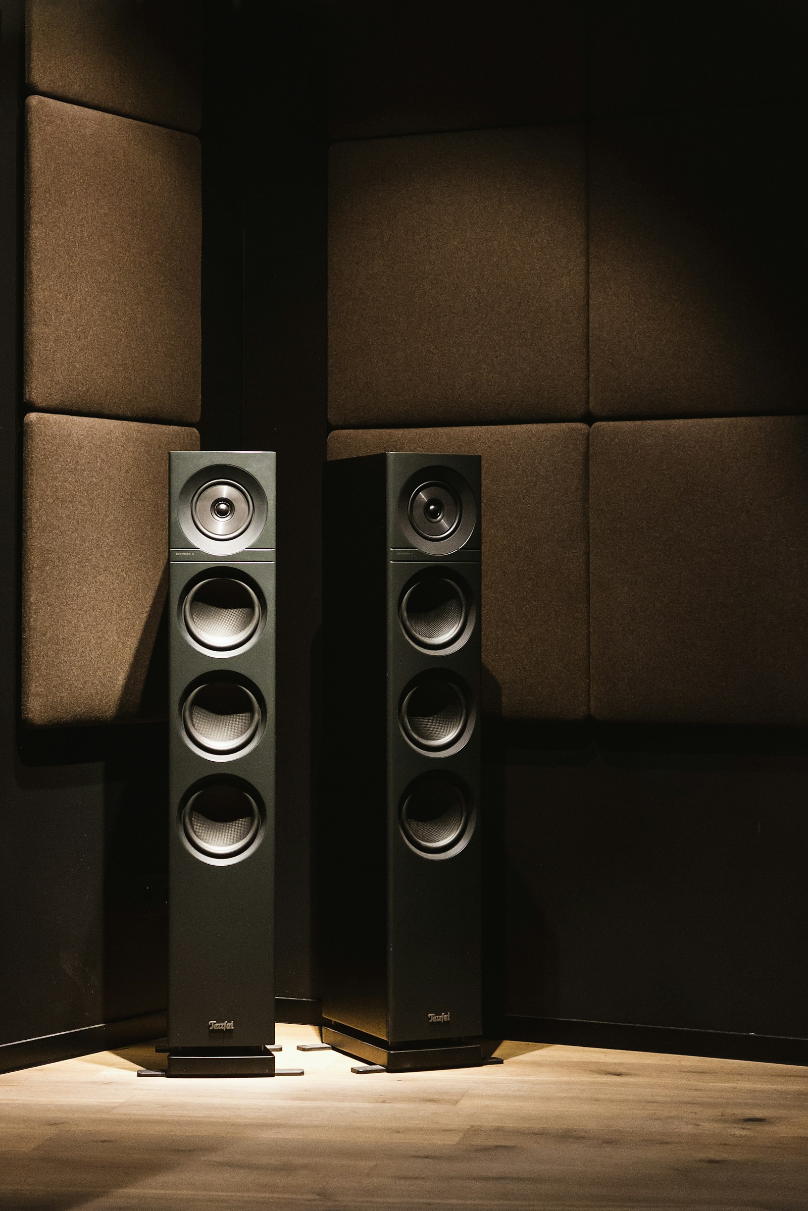 A pair of floorstanding speakers lit by a single warm downlight